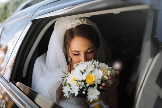 A bride is in a car with a bouquet of flowers. She is holding the bouquet and talking on her cell phone photo