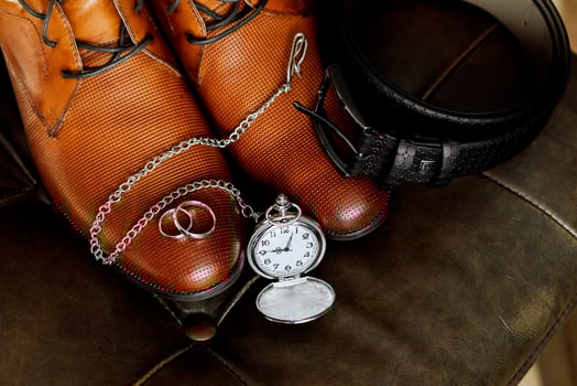 A pair of brown shoes with a silver chain and a pocket watch on top of them. The pocket watch is set to the time photo