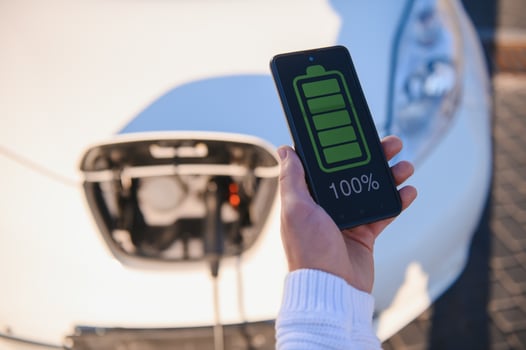 Man Charging Electric Vehicle With Cable Looking At App On Mobile Phone photo