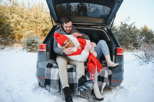 lovely smiling couple sitting in car trunk in winter forest photo