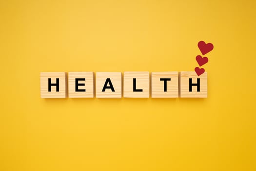 HEALTH word is written on wood blocks with three red heart symbols isolated on a yellow background. Top view. Close-up photo. Health and healthcare concept photo