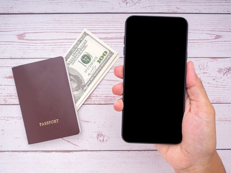 Close-up of hand holding a smartphone with passport and US dollars banknote on wooden table background. Communication and travel concept photo