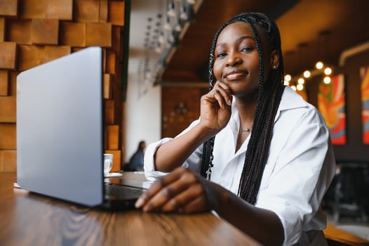 Head shot portrait of happy smiling African American woman sitting at table in cafe, looking at camera, excited female posing, working at computer, doing homework, preparing report in coffee house photo