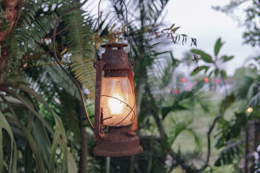 An oil lamp lantern hanging from a tree with a light inside. The lantern is old and rusted. photo