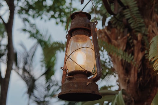 An oil lamp lantern hanging from a tree with a light inside. The lantern is old and rusted. photo