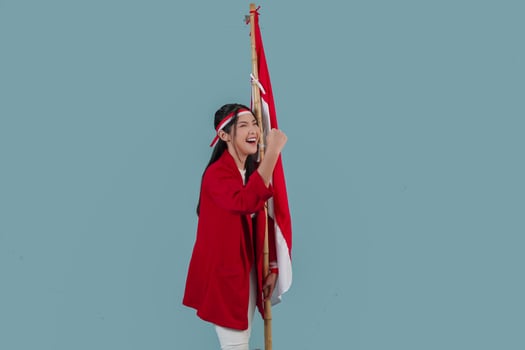 Indonesian woman wearing a red jacket holding a flag while raising fist gesture. photo