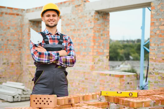 Using bricks. Young construction worker in uniform is busy at the unfinished building photo