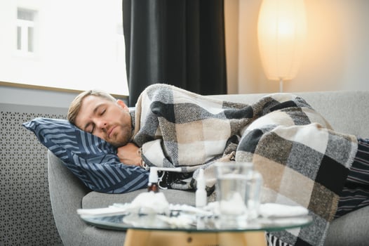 Sick bearded man who has bad cold or seasonal flu sitting on couch at home. Guy with fever wearing warm plaid shivering with worried face expression. photo