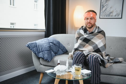 Young man suffering from cold at his home. Shot of a young man sitting on his bed while feeling unwell at home. Trying to stay warm. Sick man photo