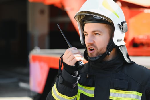 Fireman in a protective uniform standing next to a fire truck and talking on the radio. photo