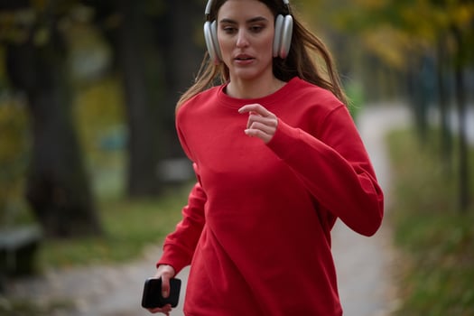 Young beautiful woman running in autumn park and listening to music with headphones on smartphone photo