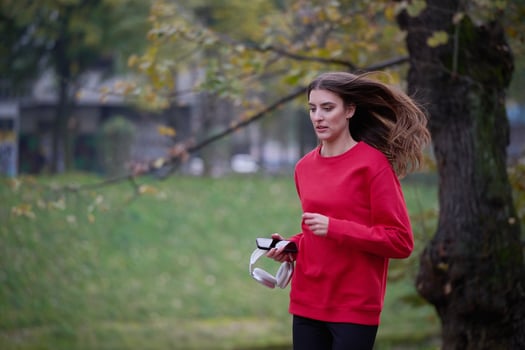 Young beautiful woman running in autumn park and listening to music with headphones on smartphone photo