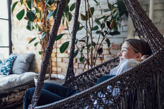 Young pretty caucasian girl lauthing and sitting in wicker chair. Blonde female teen in casual clothes is resting at home. photo