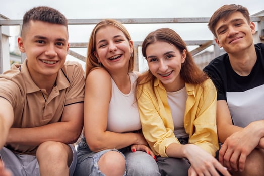 Four cute teenagers taking a selfie. Funny friends takes a picture of theyself on the phone outdoors. Smiling boys and girls sitting on the street. photo