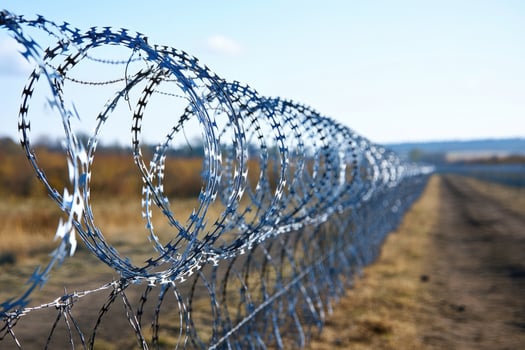 Barbed wire fence creating a secure border line under blue sky photo