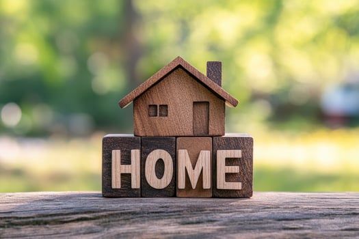 Miniature wooden house standing on top of 'home' text on blurry green background photo