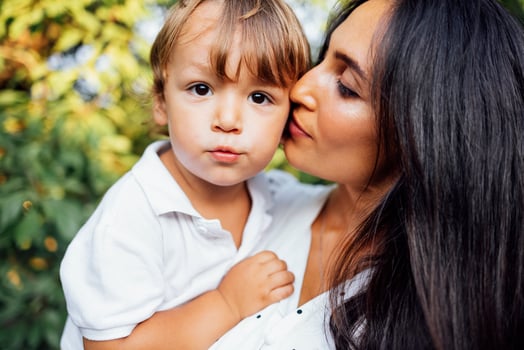 Lovely portrait of a beautiful mother kissing her little son. Close up of a young brunette female face touching to her cute child. photo