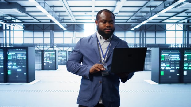 IT engineer working on laptop in modern data center, overseeing server operations, system maintenance,and cybersecurity protocols, ensuring optimal performance and data integrity, camera B photo