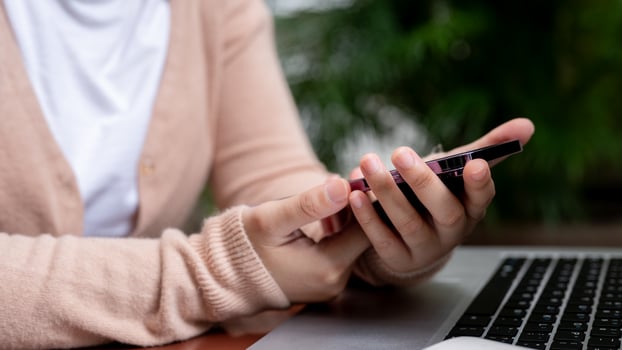 A close-up image of a woman is using her smartphone while working remotely at a table in a garden. photo