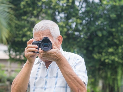 Happy senior man taking photographs with a digital camera while standing outdoors. Aged people photographer and relaxation concept photo