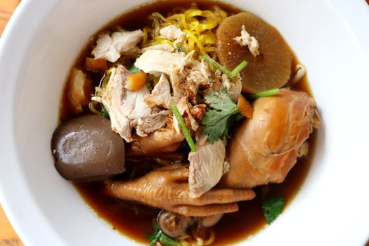 Close up top view of egg noodle in braised drumstick and feet chicken Thai style soup with blood in white bowl in Thailand. photo