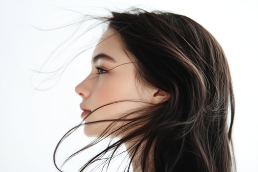 A profile portrait of a young brunette woman with flowing hair on a white background. photo