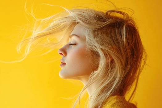Blonde woman in profile with wind-blown hair against a yellow studio background. photo