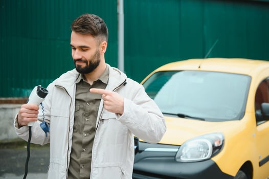 Man Holding Power Charging Cable For Electric Car In Outdoor Car Park. And he s going to connect the car to the charging station in the parking lot near the shopping center photo