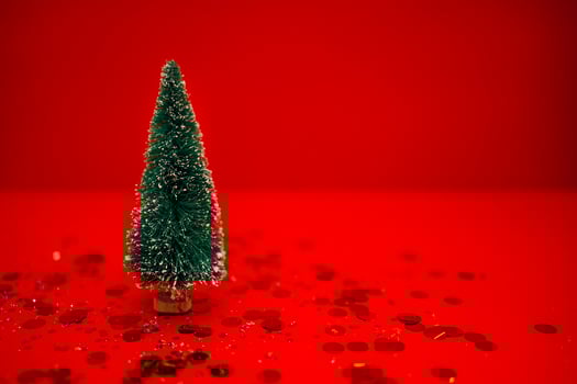Stylish little Christmas tree on a red background. Bright holiday backdrop with silver glitters and gold round confetti. photo