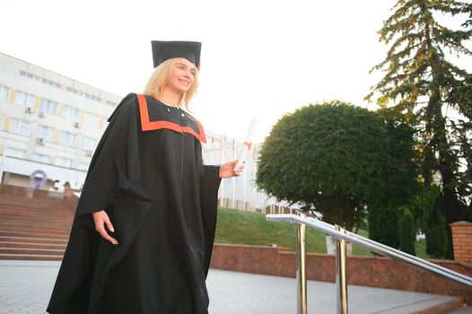 Portrait enthusiastic female college student graduate in cap and gown celebrating, holding diploma. photo