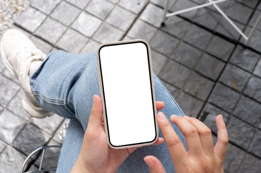 Top view image of a woman in jeans sitting outdoors, using her smartphone, touching on the screen. photo