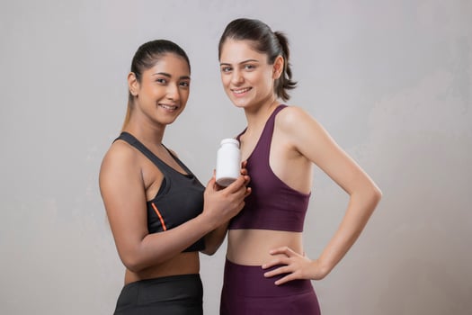 Two Gorgeous Females Are Standing And Displaying The Vitamin Bottle In Her Hand photo