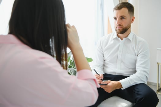 Psychologist taking notes during therapy session with sad young woman in his office. Copy space photo