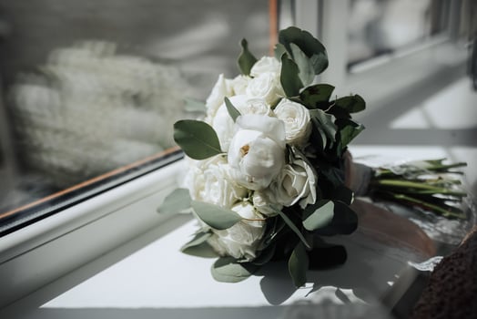 A bouquet of white flowers sits on a windowsill. The flowers are white and green, and the arrangement is simple and elegant. The bouquet is a symbol of love and affection photo
