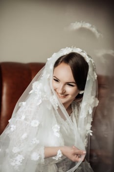 A woman in a white veil is sitting on a brown chair. She is smiling and looking at the camera photo