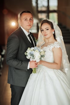 A bride and groom are posing for a picture. The bride is wearing a white dress and holding a bouquet of flowers. Concept of love and happiness photo