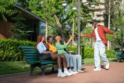Overjoyed black guy student extends hand high five to friends lounging on bench on university campus photo