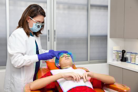 Skin lesion removal procedure. Dermatologist carrying out a removal of benign skin lesion on the face of a young male patient. photo