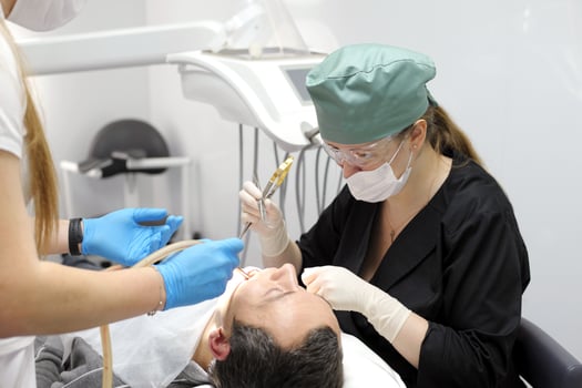 Dentist Closeup woman patient. Carious tooth treatment at dental clinic office. Nurse, doctor hand. Dentist making teeth cleaning, treating and canal filling. assistant spaying mouth photo