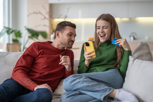 Happy married couple, spouses on couch making online purchases via internet using smartphone. photo