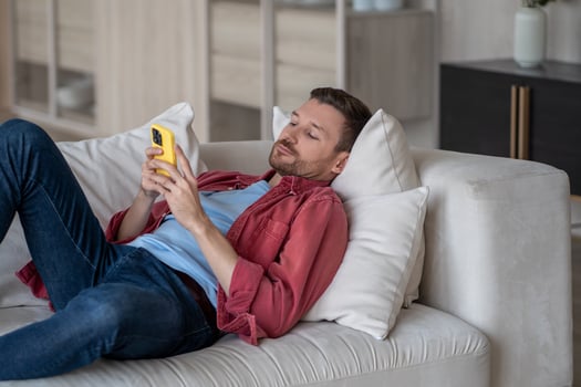 Procrastination with phone. Lazy man with social media addiction lying on couch at home scroll web photo