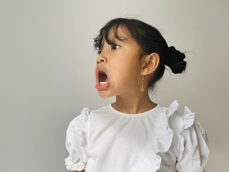 Five year old Asian little girl wearing white shirt standing showing angry gesture. Rude kids concept photo
