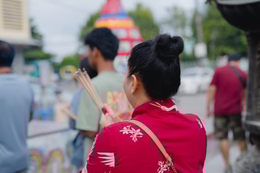 A woman in a red dress holds incense. She stands in a group of people. photo