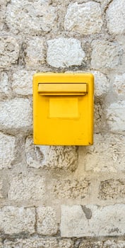 A yellow mailbox on a light stone wall. Box for letters and postcards. photo