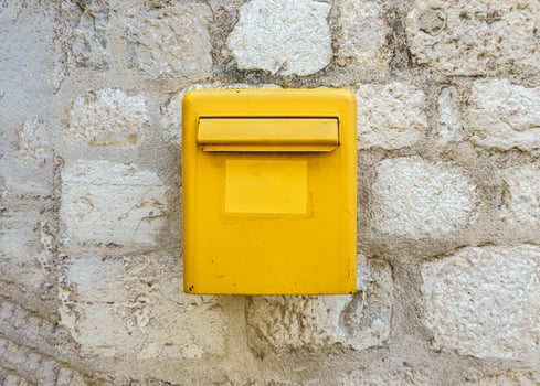 A yellow mailbox on a light stone wall. Box for letters and postcards. photo