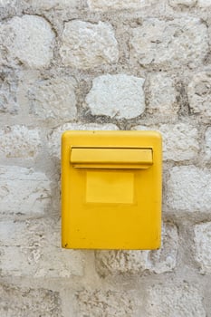 A yellow mailbox on a light stone wall. Box for letters and postcards. photo