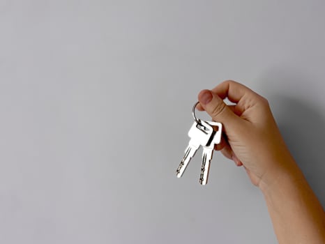 Close up of hand holding set of silver keys against plain light grey background with copy space. Minimalistic image symbolizing real estate, property ownership, or access with focus on metal keys. photo