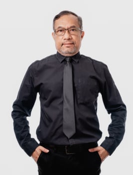 Asian man in a black shirt and tie stands with his hands in his pockets. He has a serious expression on his face photo