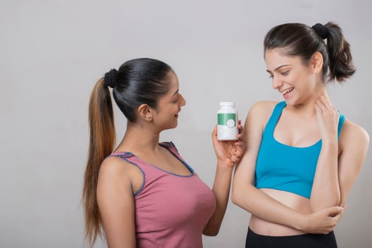 Two Beauty Ladies Are Looking Lovingly At The Tablet Bottle That One Of Them Is Holding In Her Hand photo
