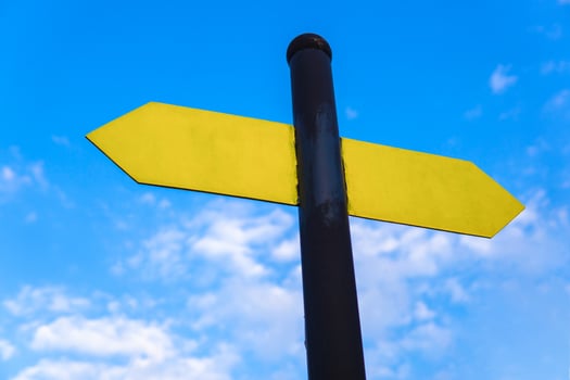 Yellow direction sign on the pole against the blue sky. Yellow arrow signal against sky. photo